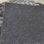 Close-up of a black rubber mat with blue and white speckles and a textured edge.