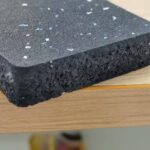 Side view of a black rubber mat with blue speckles, showing the thickness and texture