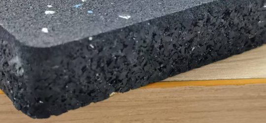 Side view of a black rubber mat with blue speckles, showing the thickness and texture